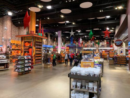 A colorful candy store interior with shelves of snacks, decorations, and shoppers browsing the aisles.