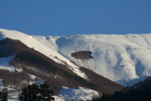 Snow-covered mountain landscape with a clear blue sky and a visible snow slide on the slope.
