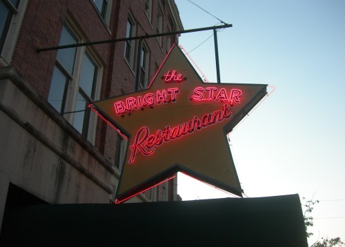 Neon sign of "The Bright Star Restaurant" in the shape of a star, illuminated against a twilight sky.