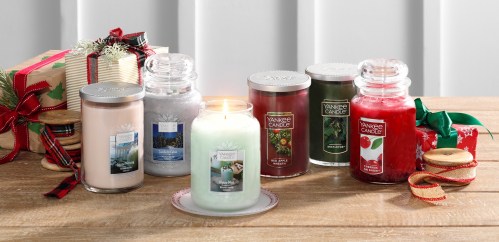 A collection of Yankee Candles in various scents displayed on a wooden table, surrounded by holiday decorations.