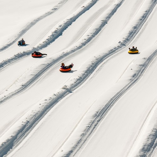Aerial view of people tubing down snowy slopes, creating wavy tracks in the fresh snow.