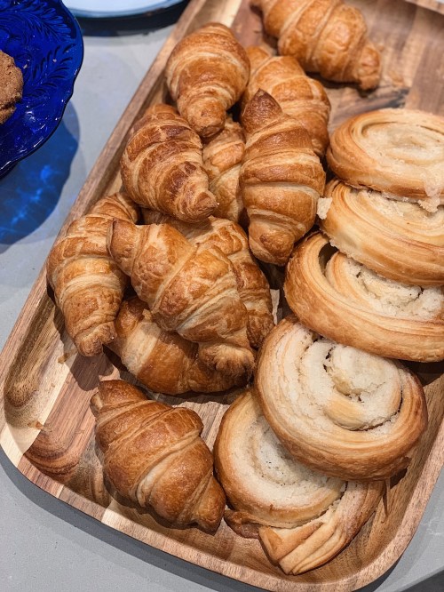 A wooden platter filled with freshly baked croissants and spiral pastries.