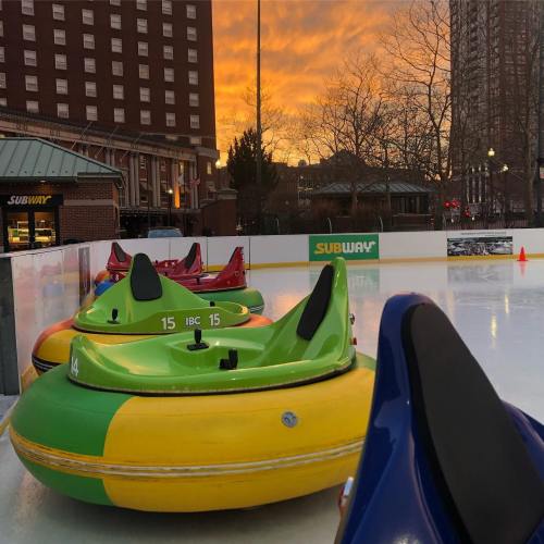 Colorful bumper boats on an ice rink with a vibrant sunset in the background.