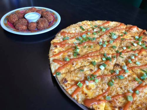 A pizza topped with green onions and drizzled with sauce, alongside a plate of golden-brown appetizers and dipping sauce.