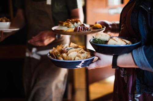 A person holds two plates of food, one with chips and the other with various appetizers, in a cozy restaurant setting.