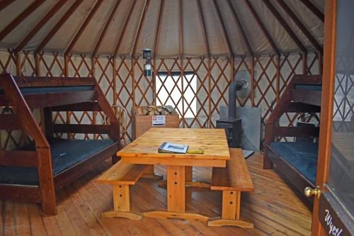 Interior of a yurt featuring wooden bunk beds, a table, and a wood stove, with a warm, rustic atmosphere.