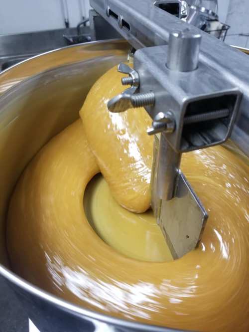 A close-up of a mixing machine blending a thick, golden substance in a large metal bowl.