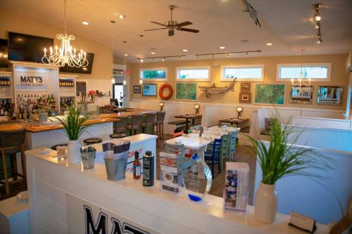 Interior of a cozy restaurant with a bar, tables, and nautical decor, featuring a chandelier and vibrant artwork.