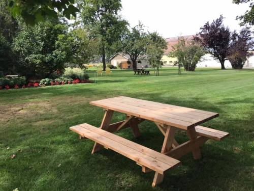 A wooden picnic table on a grassy lawn, surrounded by trees and flower beds in a serene outdoor setting.