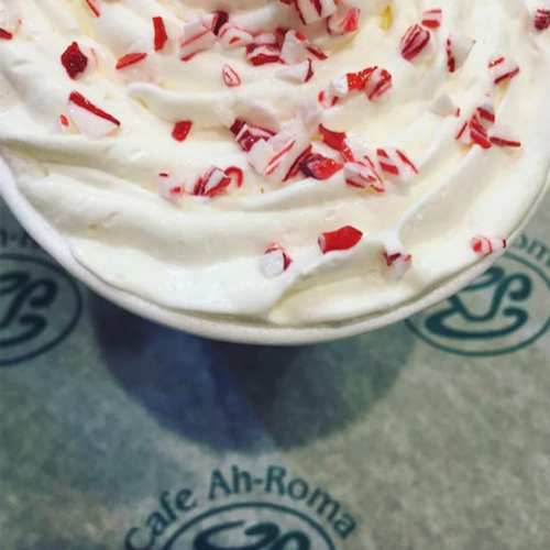 A close-up of a cup of whipped cream topped with crushed peppermint candies on a branded paper surface.