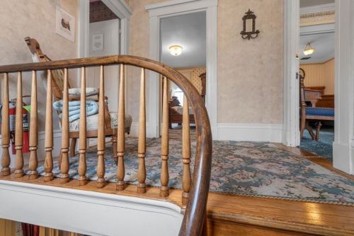 A cozy hallway with a wooden railing, patterned carpet, and a glimpse of a room in the background.