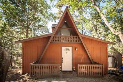 A charming A-frame cabin surrounded by trees, featuring a front porch and a welcoming entrance.