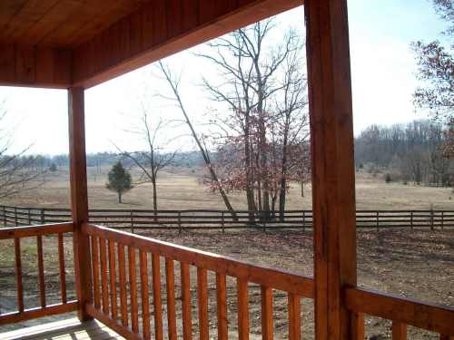 View from a wooden porch overlooking a grassy field and trees under a clear sky.