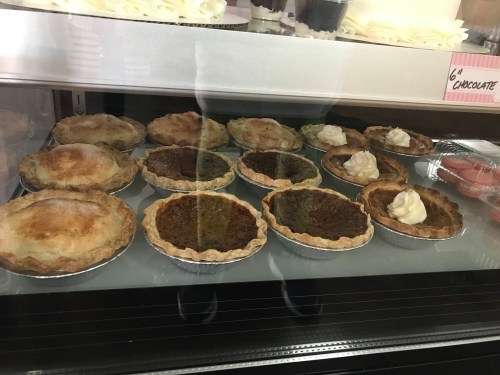 A display case filled with various small pies, some topped with whipped cream, showcasing different crusts and fillings.