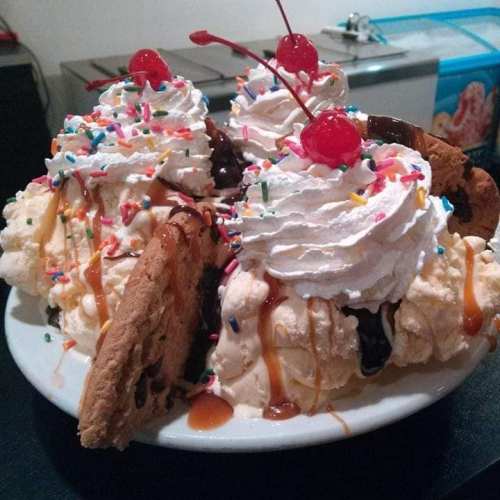 A large dessert bowl filled with ice cream, whipped cream, sprinkles, cookies, and cherries on top.