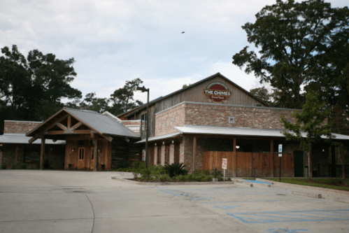 Exterior view of The Chimes restaurant, featuring a rustic design with brick and wood elements, surrounded by trees.