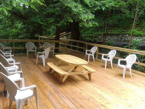 A wooden deck surrounded by trees, featuring a picnic table and several white chairs arranged around it.