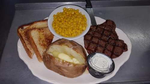 A plate with grilled steak, a baked potato with butter, corn, and two slices of toasted bread.