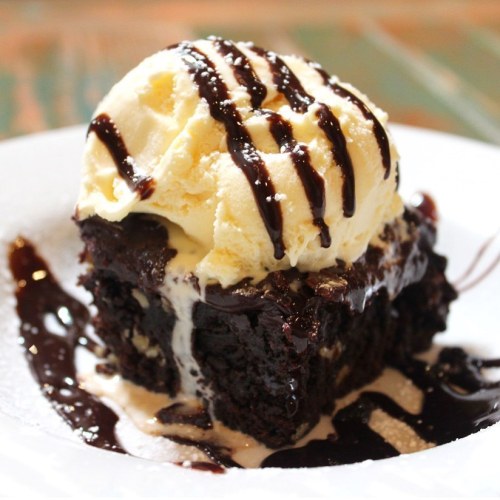 A decadent chocolate brownie topped with vanilla ice cream and drizzled with chocolate sauce on a white plate.