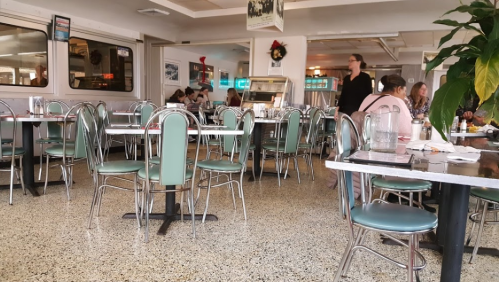 A retro diner interior with green chairs, tables, and a few patrons dining in a casual atmosphere.