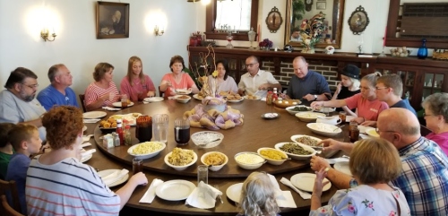 A large group of people gathered around a table filled with various dishes, enjoying a meal together in a cozy setting.