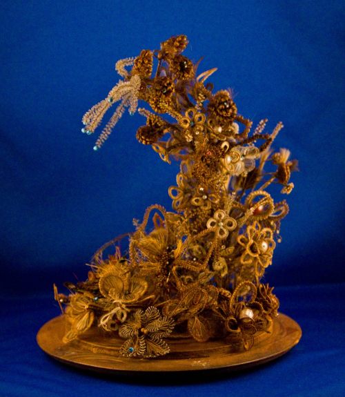 A decorative arrangement of intricate golden flowers and foliage on a circular base against a blue background.