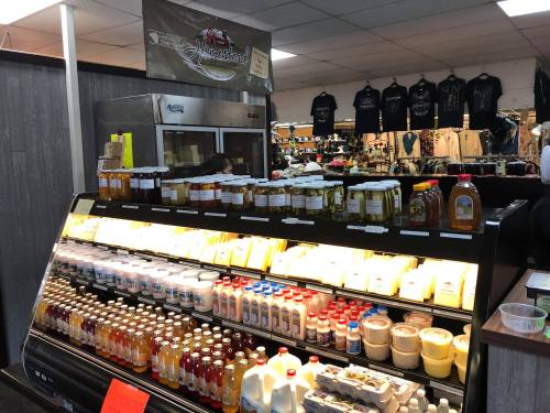 A display of various dairy products, honey, and beverages in a market, with merchandise hanging in the background.