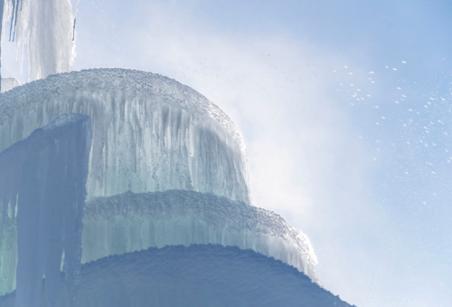 A close-up of icy formations with layered textures against a bright blue sky.