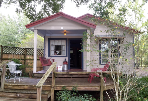 A cozy house with a red roof, porch, and wooden deck surrounded by greenery and outdoor seating.