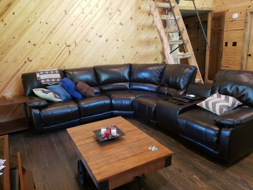 A cozy living room featuring a black leather sectional sofa and a wooden coffee table in a cabin-like setting.