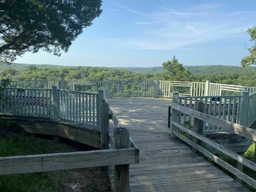 A wooden observation deck overlooks a lush green landscape under a clear blue sky.
