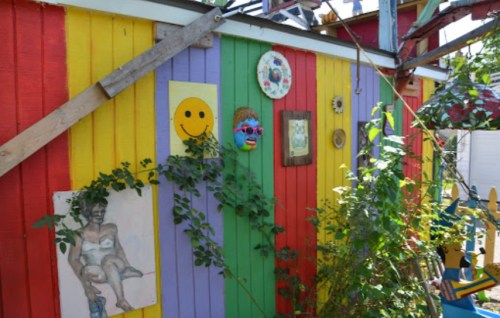 Colorful wall with yellow, purple, and red panels, featuring art, a smiling face, and greenery.
