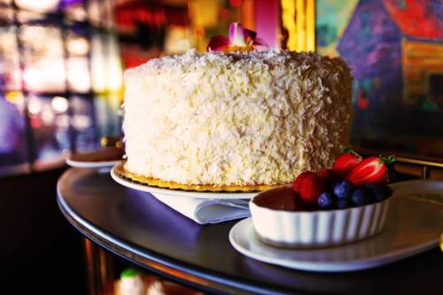 A beautifully decorated coconut cake with a flower on top, accompanied by a dish of mixed berries and chocolate mousse.