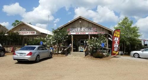 A rustic general store with a sign for live crawfish, surrounded by trees and parked cars under a blue sky.