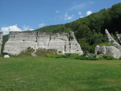 A grassy area with large, white rock formations and green hills in the background under a blue sky with clouds.