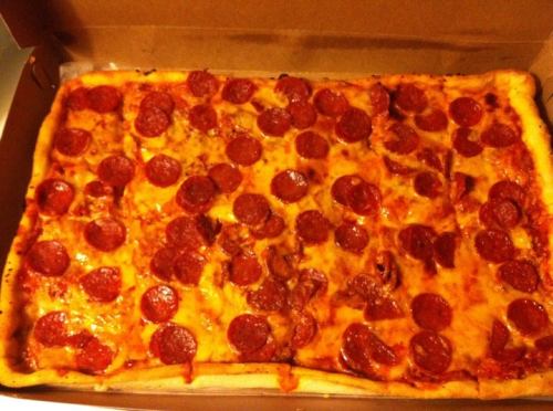 A rectangular pizza topped with numerous slices of pepperoni, inside a pizza box.