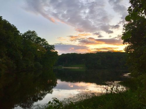 A serene lake at sunset, with colorful clouds reflecting on the water and lush greenery surrounding the scene.