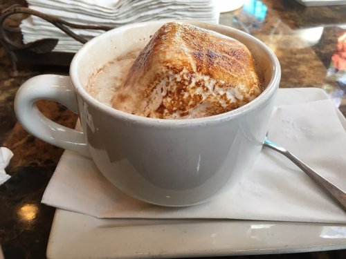 A large mug filled with hot chocolate topped with a toasted marshmallow. A spoon rests beside it on a napkin.