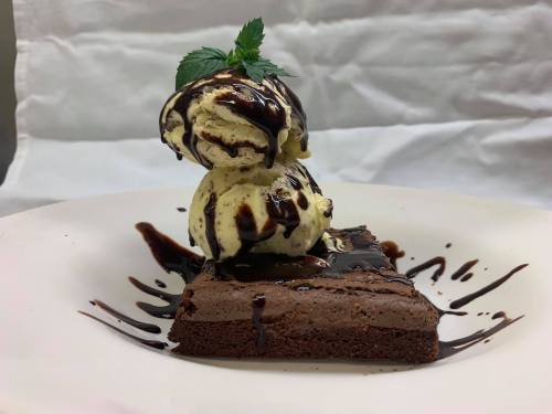 A rich chocolate brownie topped with two scoops of vanilla ice cream drizzled with chocolate sauce and garnished with mint.