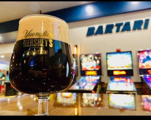 A glass of Yuengling Hershey's Chocolate Porter on a bar counter, with pinball machines in the background.