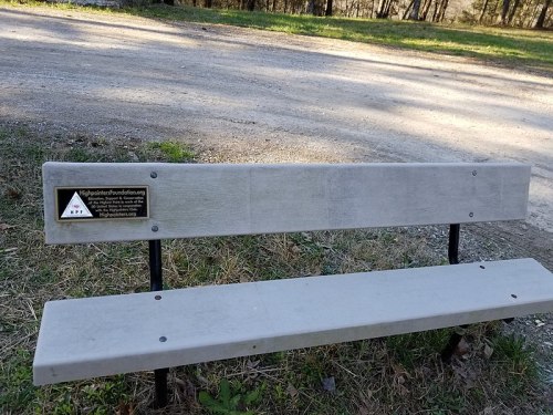 A gray bench in a park with a plaque for the Hope Is Here Foundation, surrounded by grass and trees.