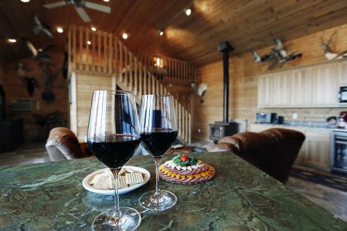 Two glasses of red wine on a marble table, with a plate of crackers and a colorful snack platter in a cozy wooden room.