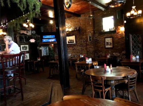 A cozy restaurant interior with wooden tables, chairs, and brick walls, featuring dim lighting and a few patrons.