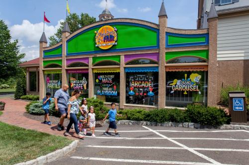 A family walks past a colorful amusement center with signs for parties, a café, an arcade, and a carousel.
