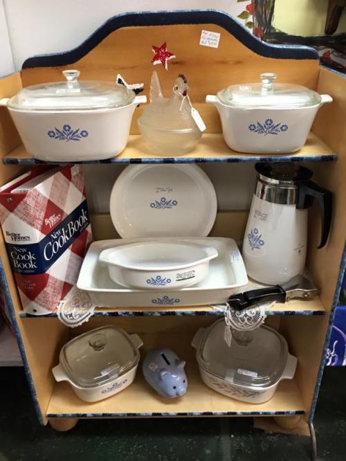 A wooden shelf displaying various vintage kitchenware, including dishes, a coffee pot, and a cookbook.