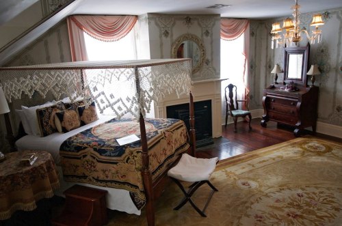 A cozy bedroom featuring a four-poster bed, vintage decor, a fireplace, and elegant furnishings.
