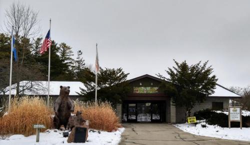Entrance of a zoo featuring bear statues, flags, and snow-covered landscaping under a cloudy sky.
