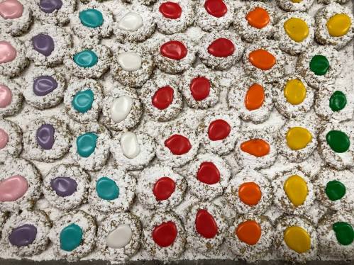 A colorful array of cookies topped with vibrant icing, arranged in neat rows on a powdered sugar-covered surface.