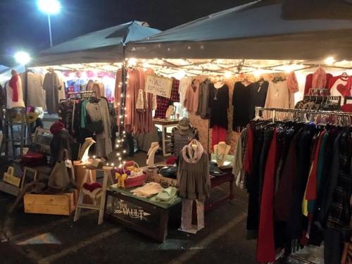 A nighttime market stall adorned with lights, displaying various clothing items and accessories on racks and tables.