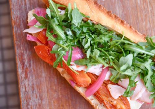 A close-up of a sandwich filled with arugula, pickled onions, tomatoes, and sliced chicken on crusty bread.